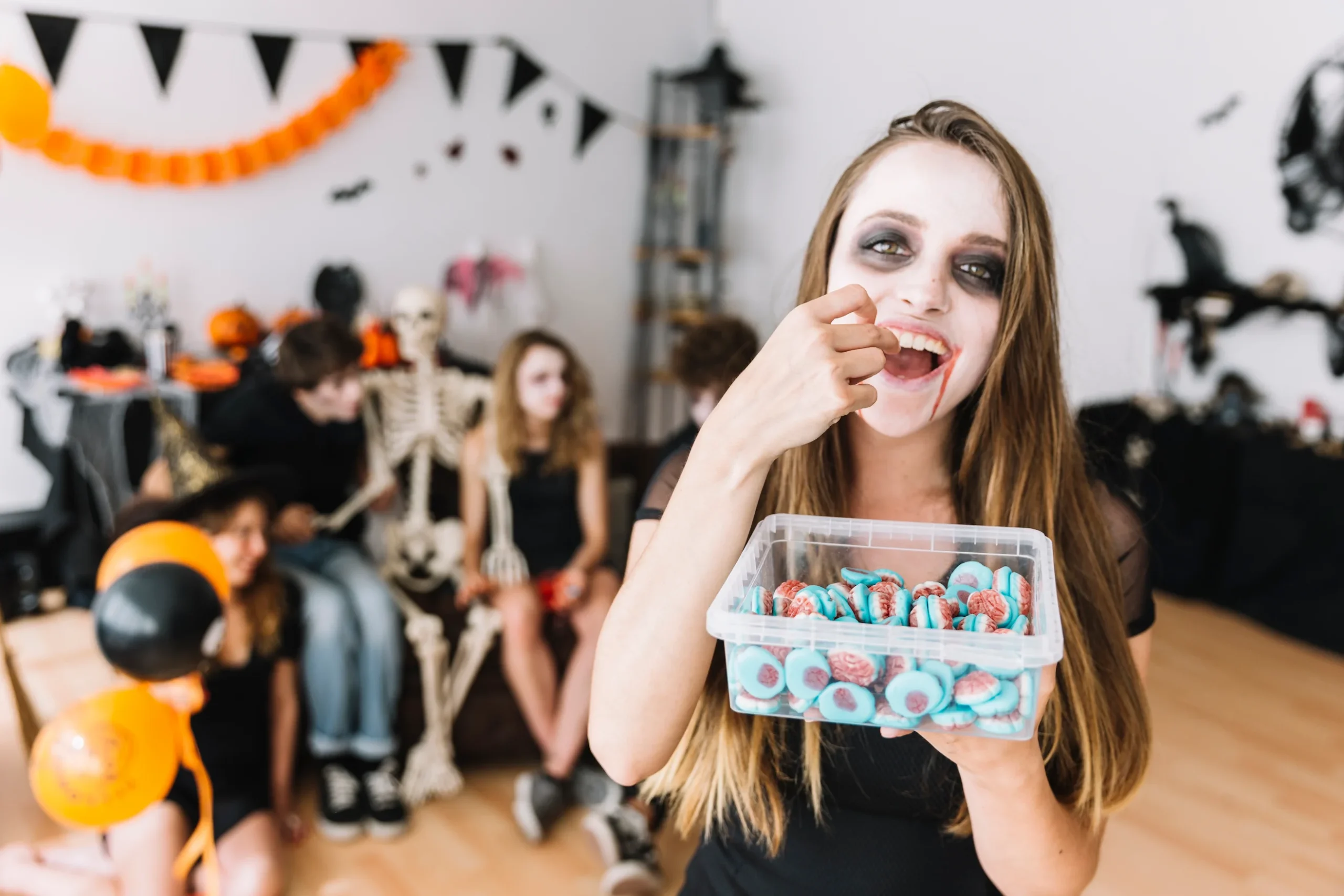 Joven disfrazada en una fiesta de Halloween comiendo dulces pegajosos, con otros niños disfrazados al fondo; representa el riesgo de caries por consumo de dulces en Halloween.